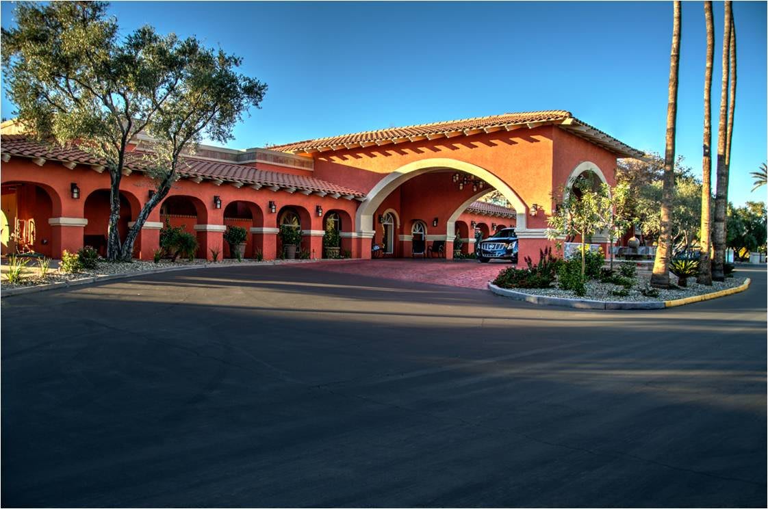A Mediterranean-style hotel entrance with a landscaped driveway and arched portico.