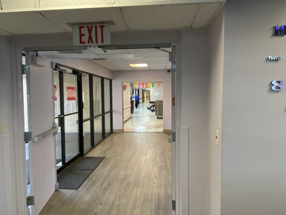A hallway in a hospital or office building featuring an exit sign and glass doors.
