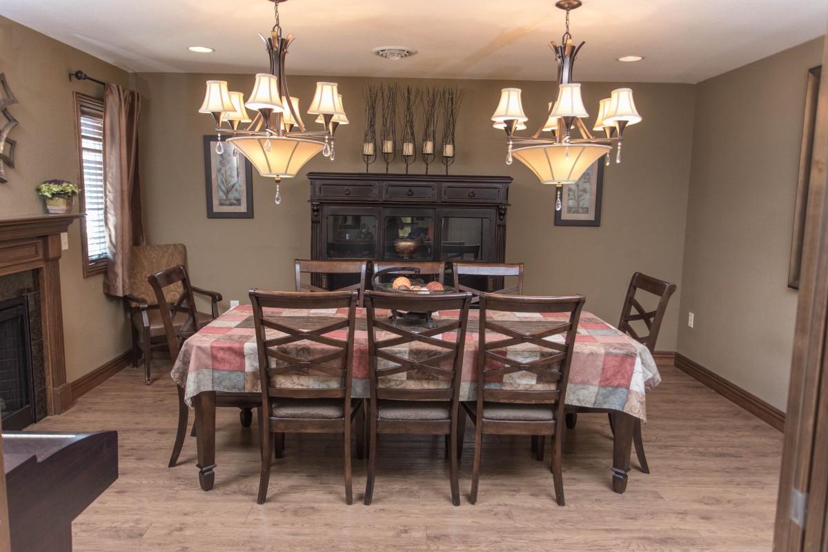 A dining room with a wooden table and six chairs, illuminated by elegant chandeliers.