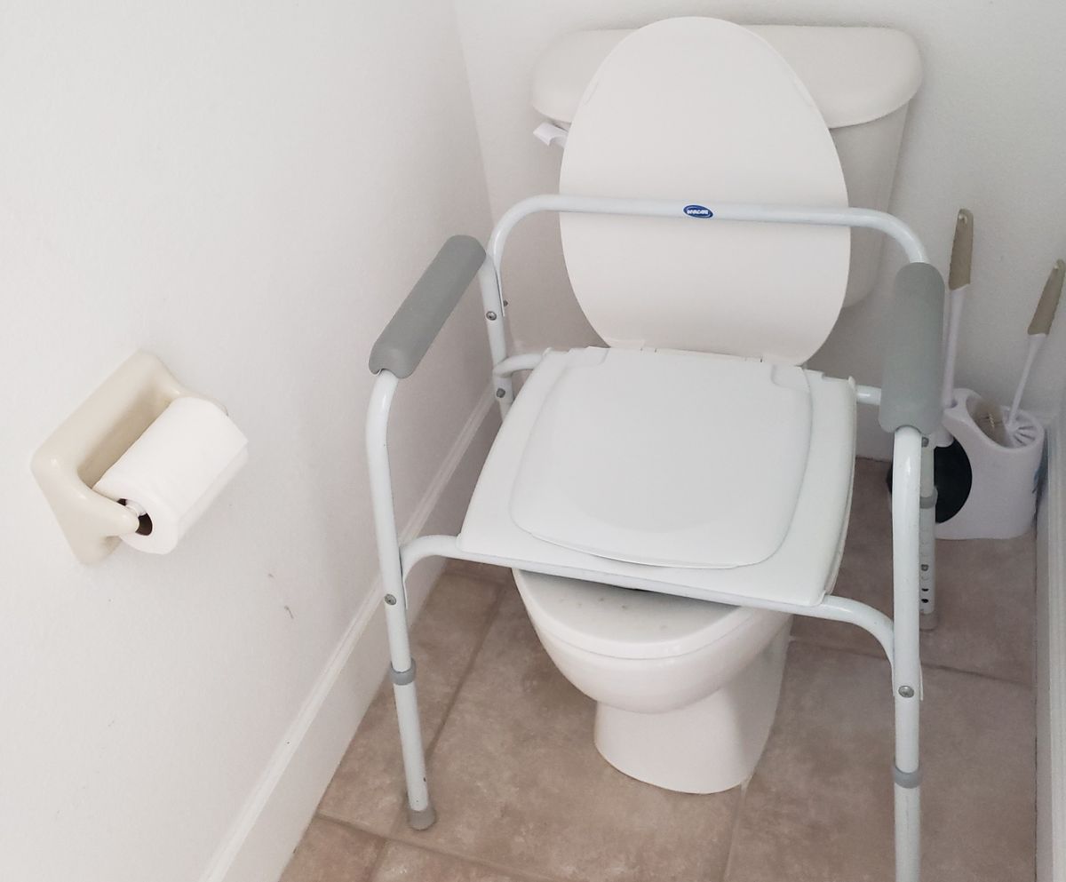 A bathroom equipped with a raised toilet seat and support frame for accessibility.