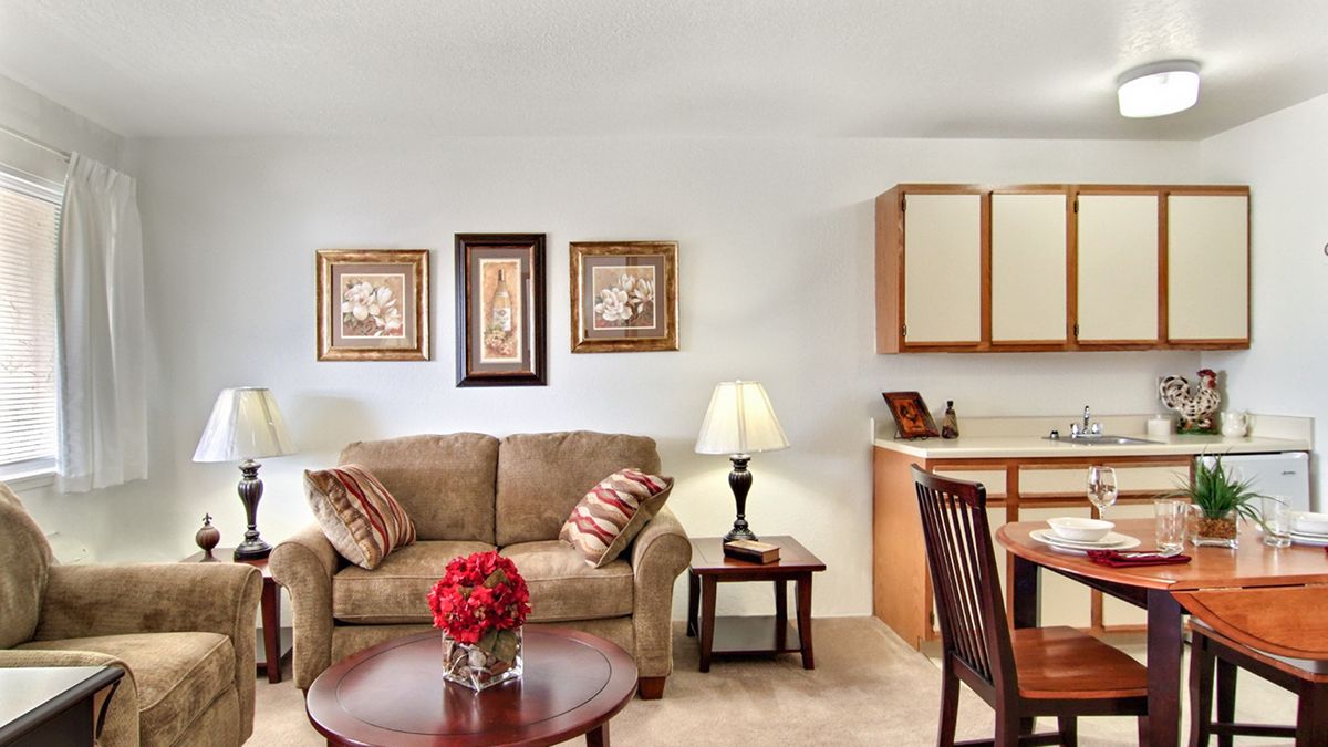 A cozy living room with a comfortable sofa, coffee table adorned with flowers, and dining area in the background.