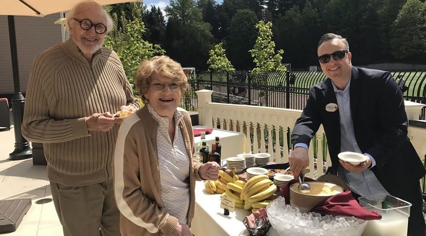 A group of people enjoying an outdoor gathering with a buffet table of food in a sunny setting.