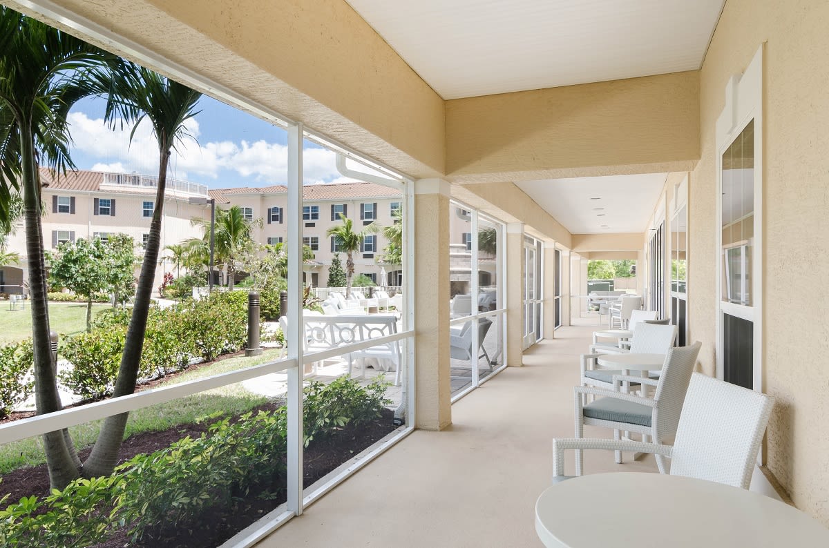 A spacious outdoor patio with white seating, offering a garden view through large windows.