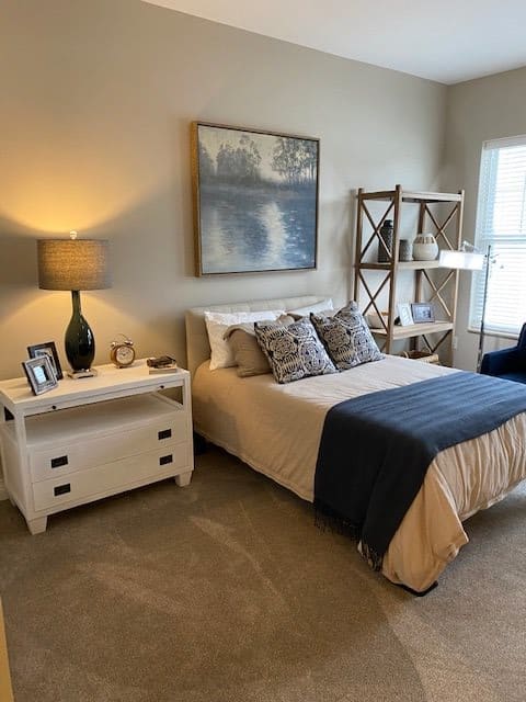 A cozy bedroom with a neatly made bed, side table with a lamp, and decorative shelves.