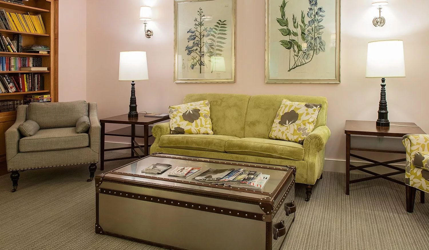 A cozy living room with a green sofa, a unique trunk-style coffee table, and botanical artwork on the wall.