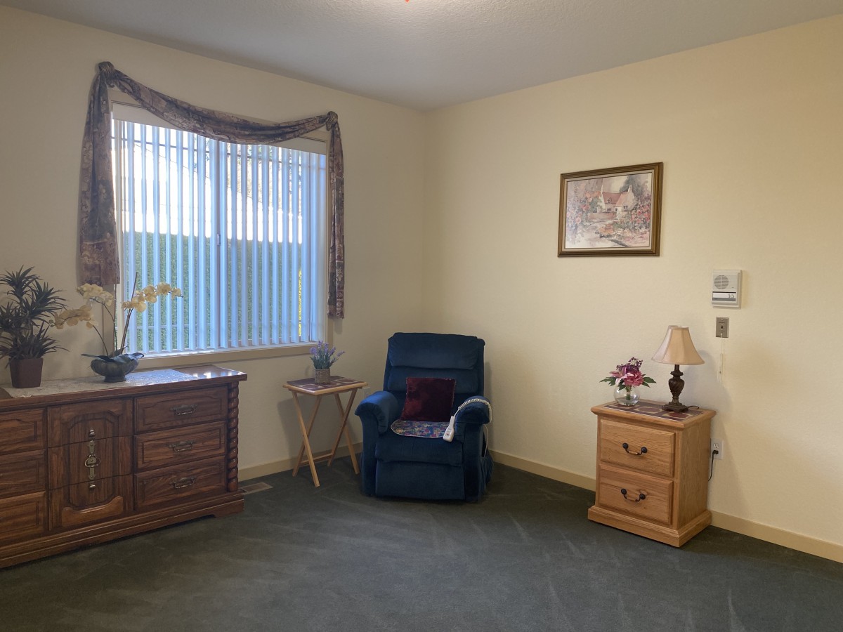 A cozy living room with a blue chair, wooden furniture, and a large window.
