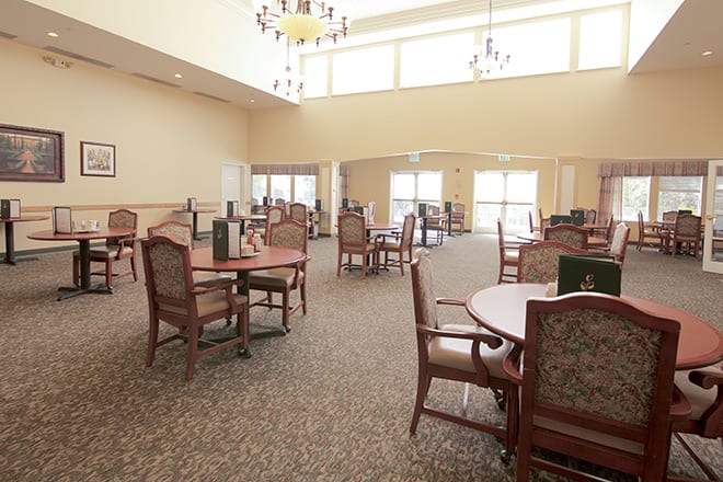 A spacious dining area with multiple tables and chairs, featuring large windows and chandeliers.