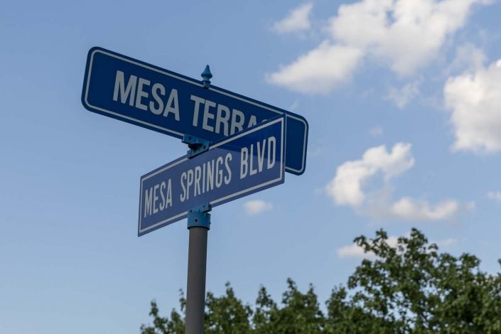 Street signs at the intersection of Mesa Terra and Mesa Springs Blvd against a backdrop of a partly cloudy sky.