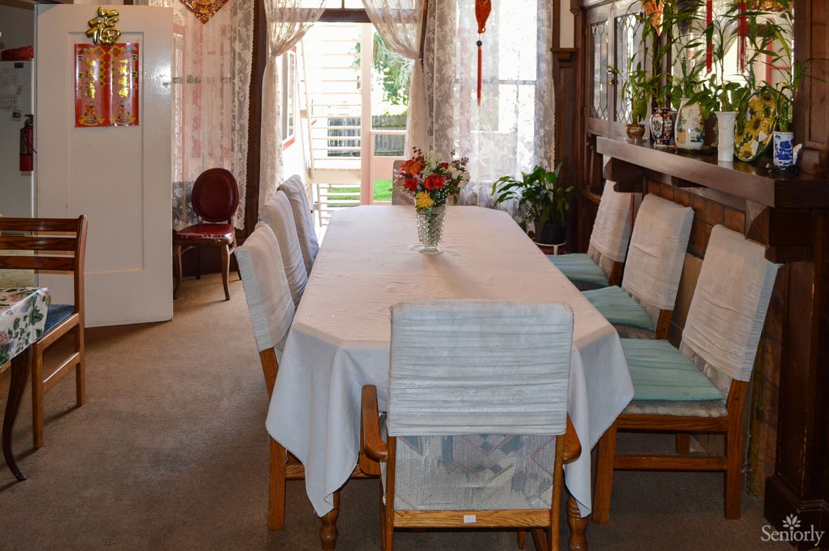 A cozy dining room with a table covered by a white tablecloth, surrounded by chairs and adorned with a vase of flowers.