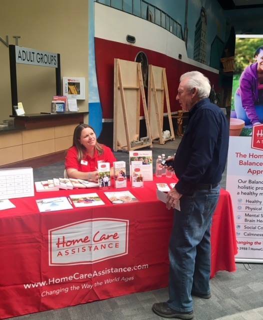 A representative at a healthcare assistance booth engaging with a visitor at an event.
