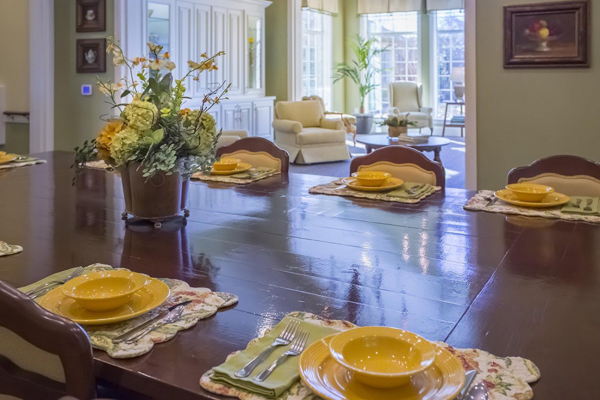 A bright dining room with a neatly set table, adorned with flowers and yellow dishware.