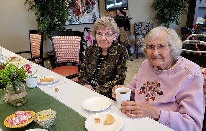 Two elderly women enjoying a meal and coffee at a community gathering.