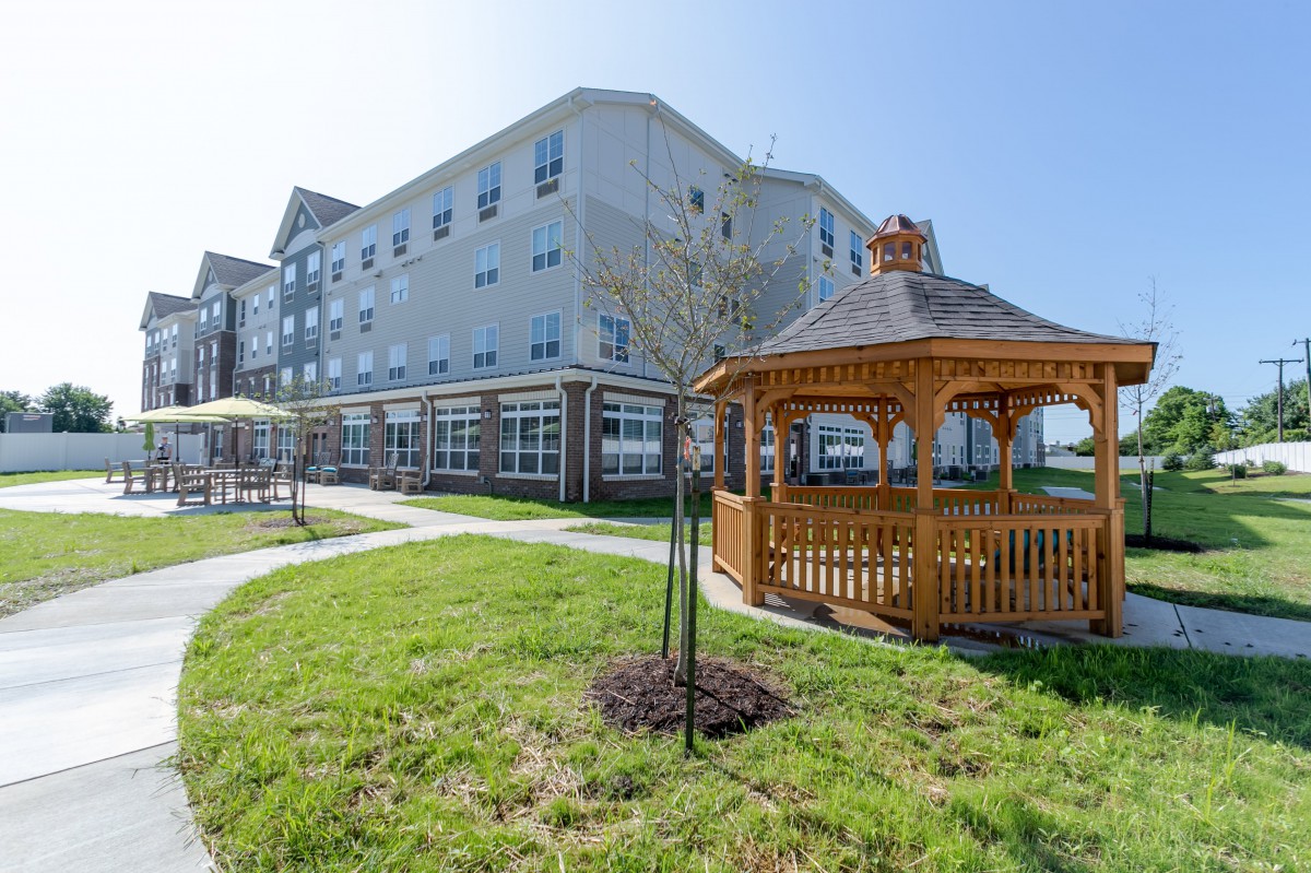 A modern multi-story building with a landscaped lawn and a wooden gazebo.