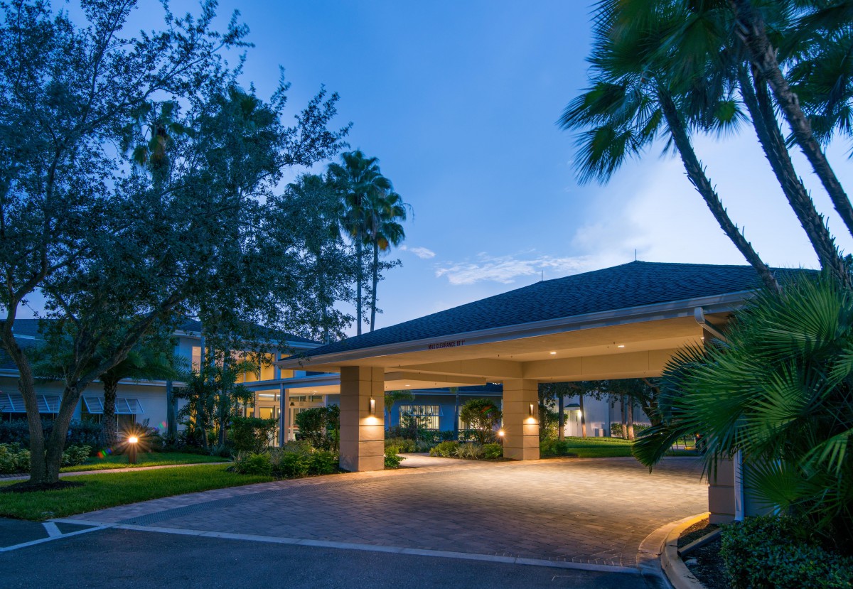 Illuminated building entrance surrounded by palm trees in the evening.