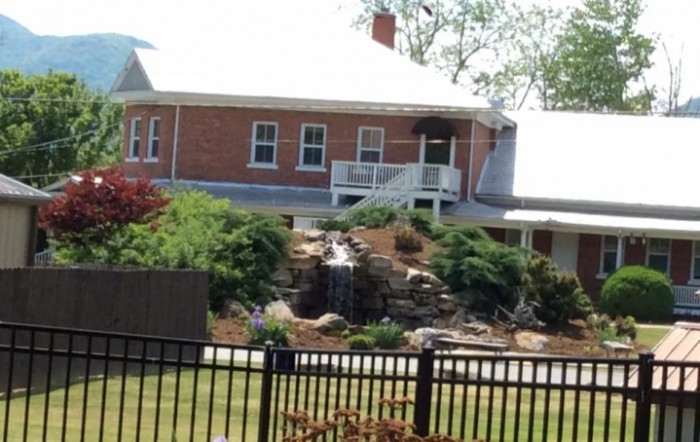 A brick house with a landscaped garden featuring a waterfall, surrounded by a fence.