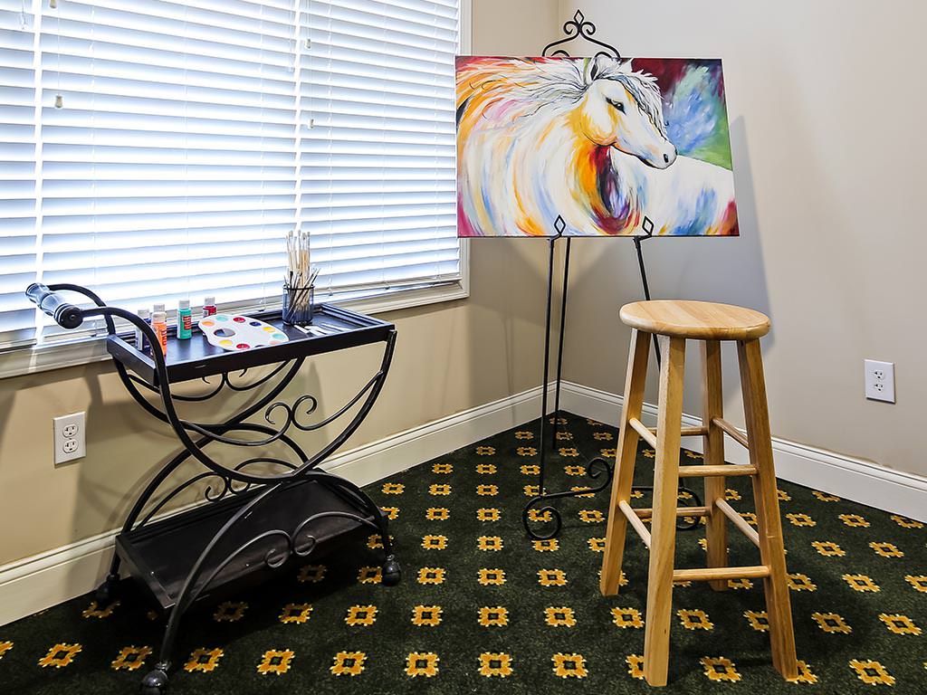 A cozy art studio corner featuring a colorful horse painting on an easel, accompanied by a stool and art supplies.