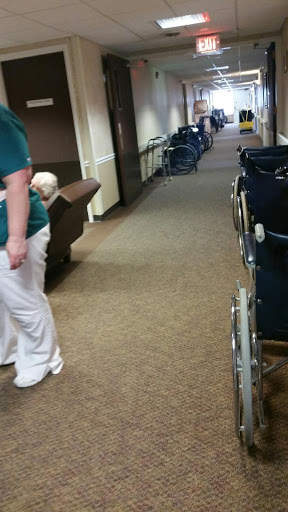 A healthcare worker attending to residents in a hallway equipped with wheelchairs.