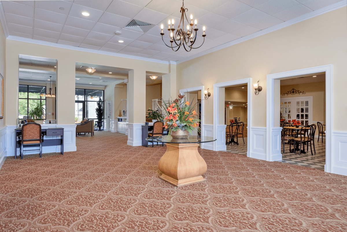 A spacious and elegantly decorated lobby featuring a chandelier and a table with a flower arrangement.