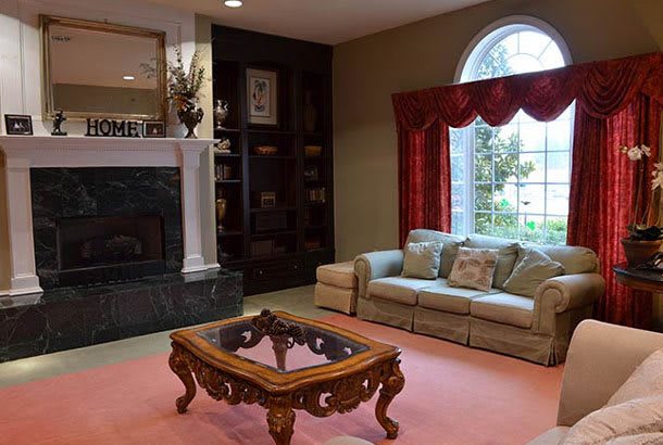 A cozy living room featuring a sofa, fireplace, and ornate coffee table with large window curtains.