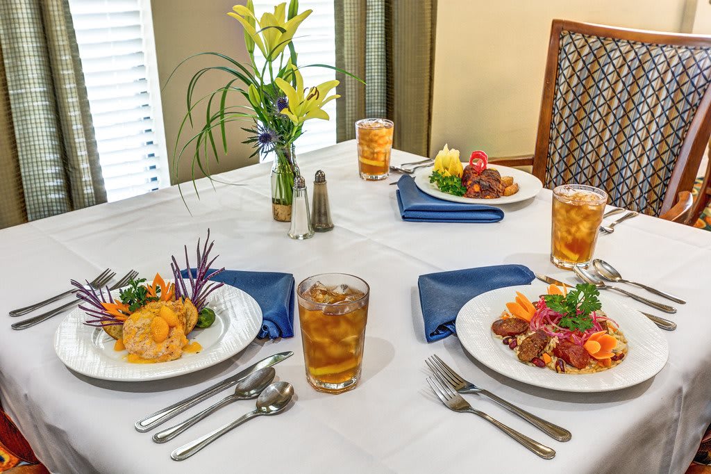 A neatly set dining table with two meals, iced tea, and a floral arrangement.