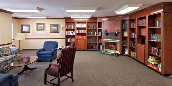 A cozy library interior with bookshelves, armchairs, and a fireplace.