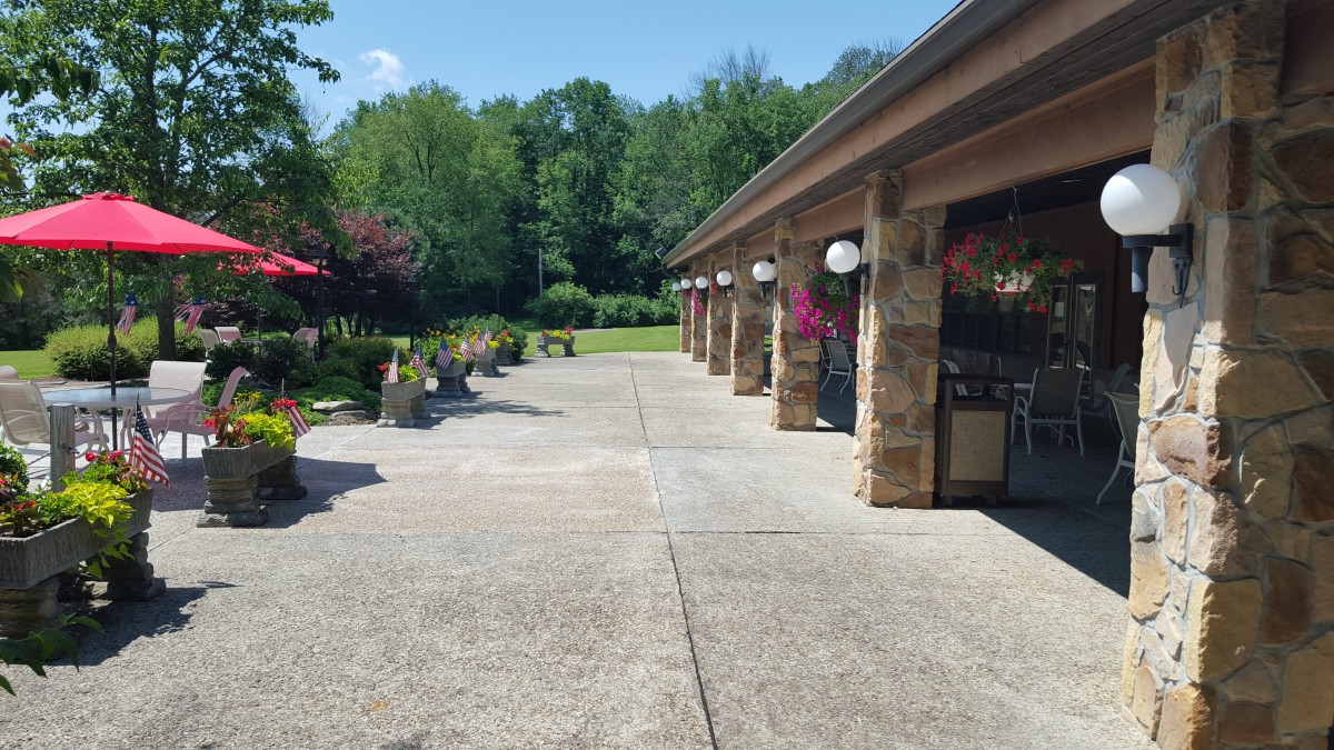 A sunny day view of a walkway beside a building, surrounded by greenery.