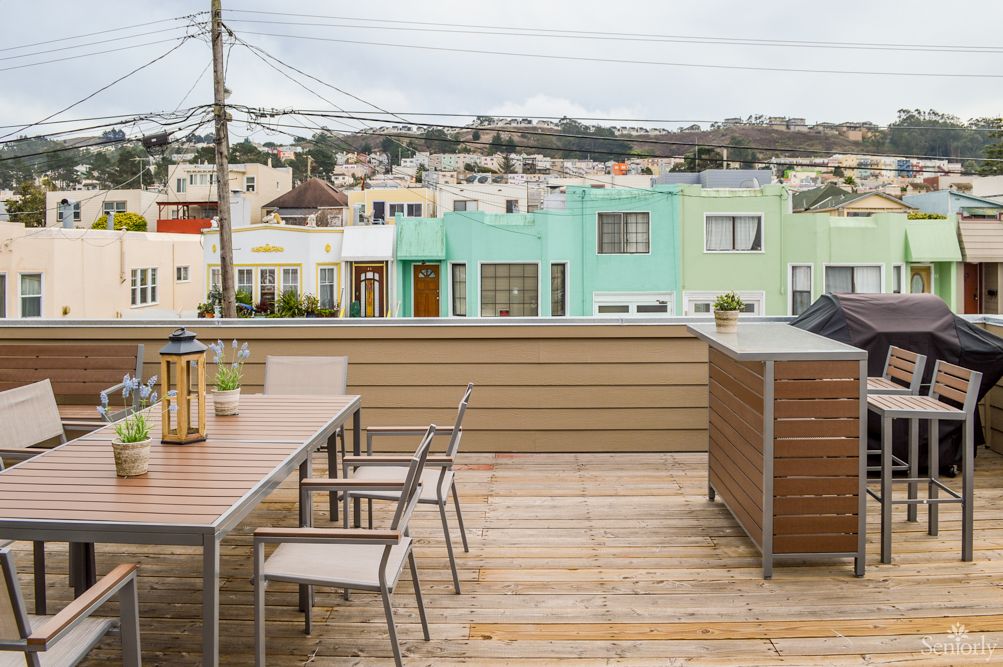 A rooftop deck with outdoor furniture overlooks colorful urban houses.
