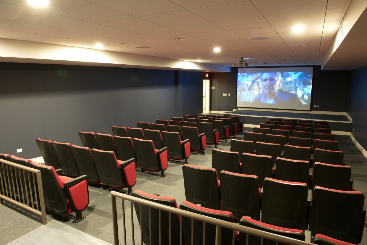 An empty movie theater with rows of seats facing a large screen.