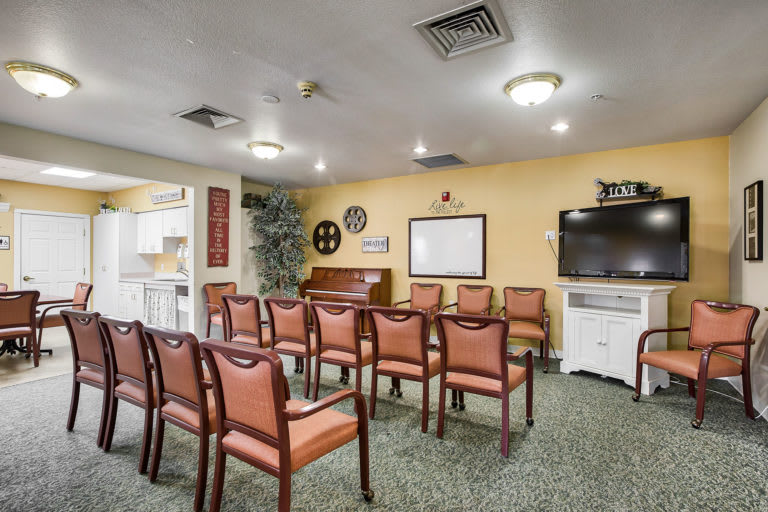 A cozy meeting room with rows of chairs facing a television and whiteboard, set up for a lecture or presentation.