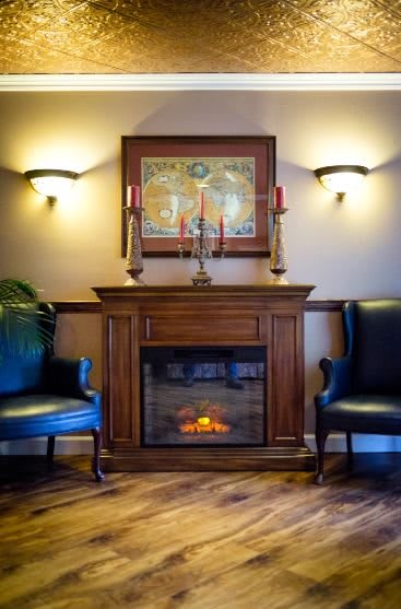 A cozy living room with a wooden fireplace flanked by two blue armchairs and adorned with artwork and candleholders.