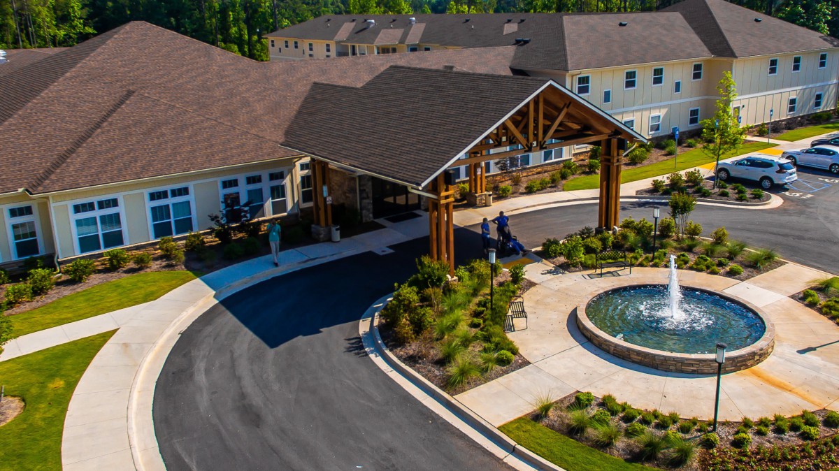 Aerial view of a residential building entrance with landscaped gardens and a circular driveway featuring a fountain.