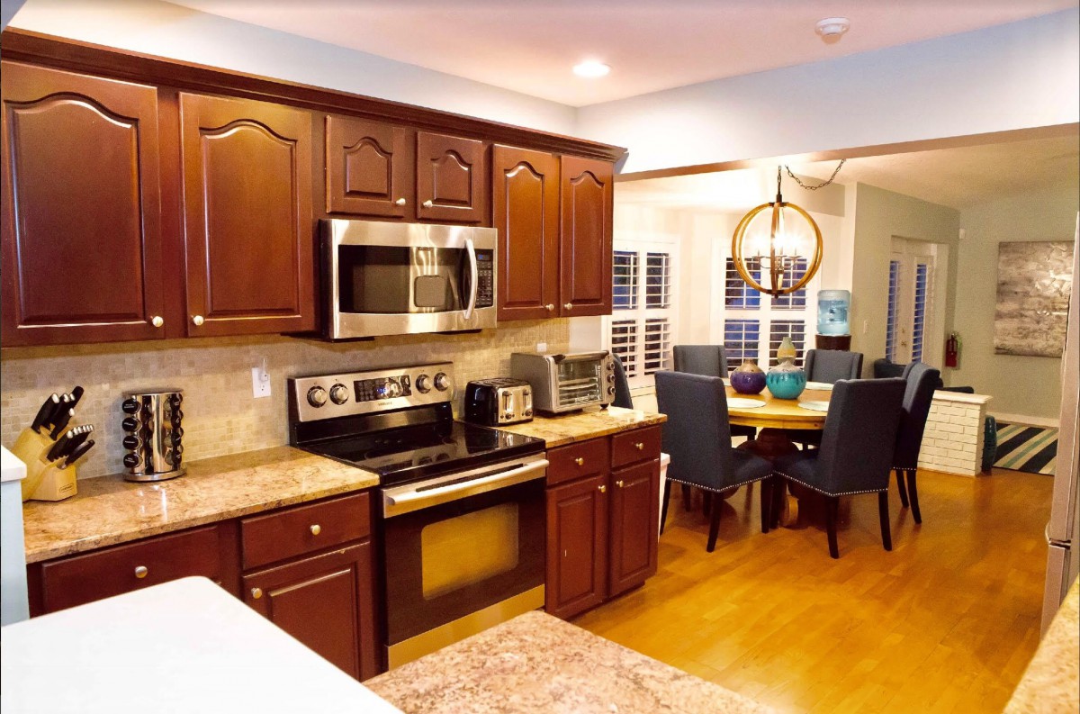 A modern kitchen with wood cabinets and stainless steel appliances, featuring an open layout adjacent to a dining area.