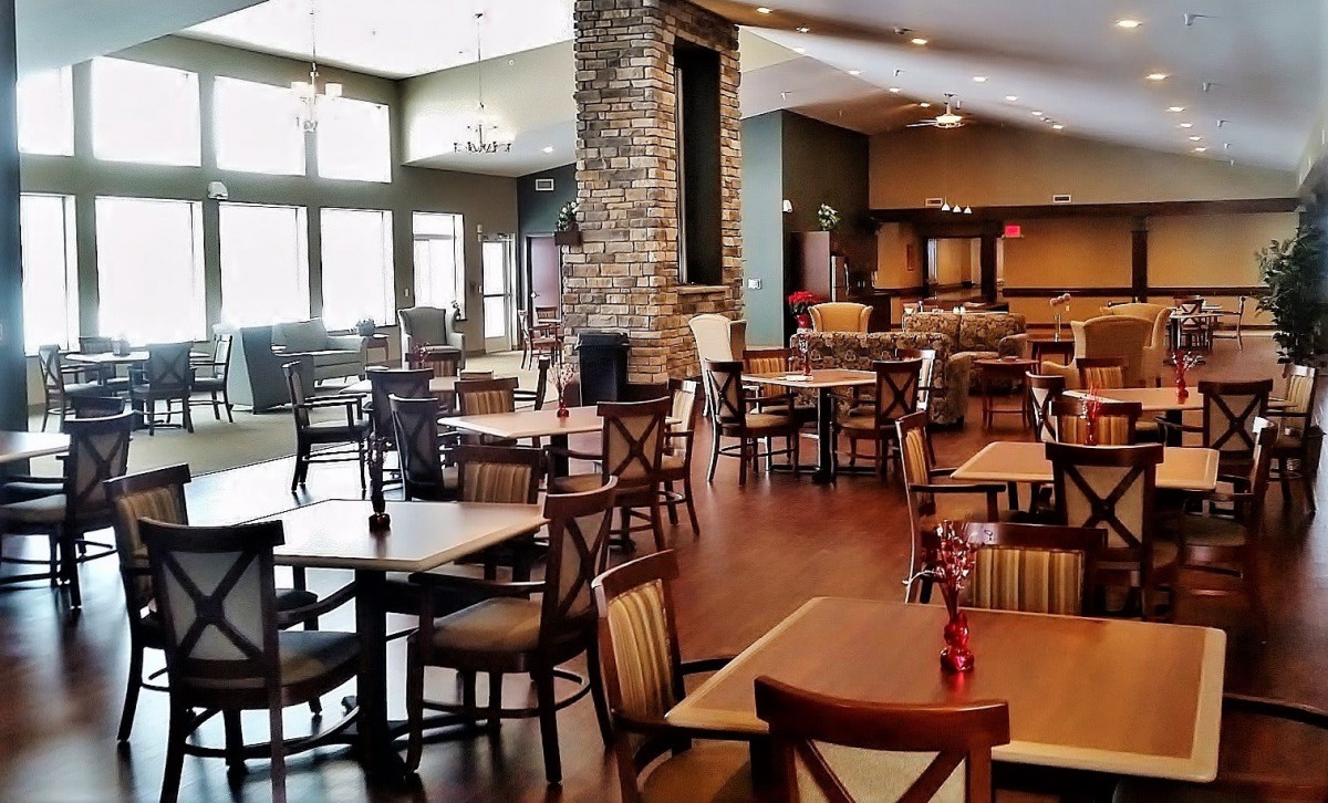 An empty restaurant dining area with tables, chairs, a brick wall, and natural lighting.