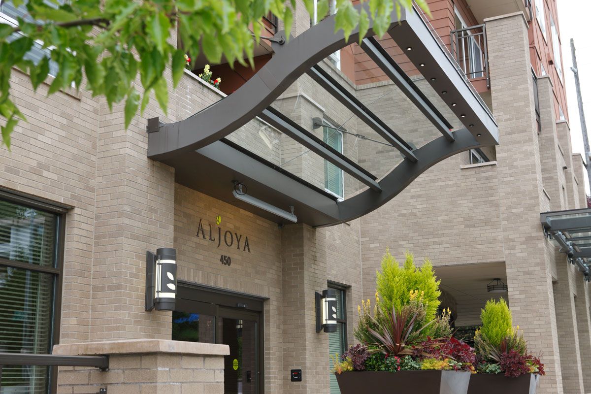 Modern building entrance with a glass awning and potted plants.