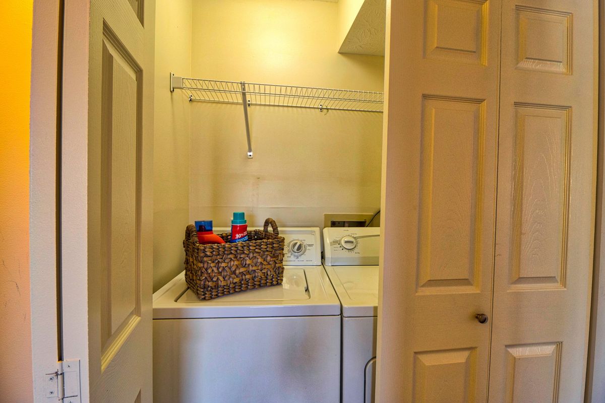 A compact laundry room with a washer and dryer, featuring a basket of detergents on top.