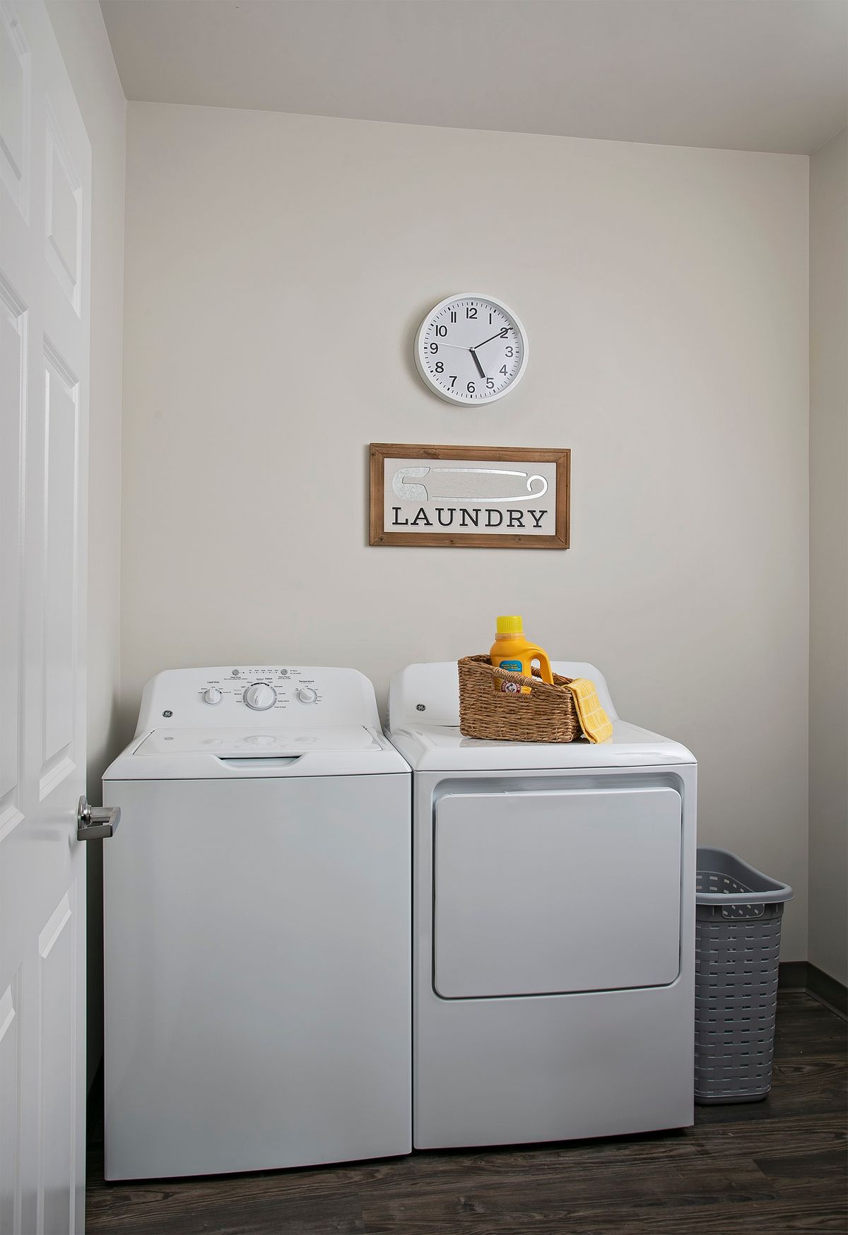 A tidy laundry room with a washing machine and dryer under a wall clock.