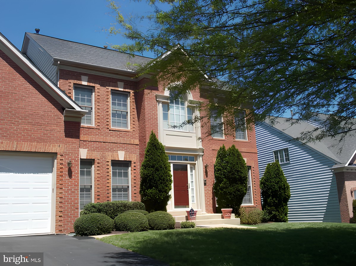 A suburban brick house with trees and bushes on a sunny day.