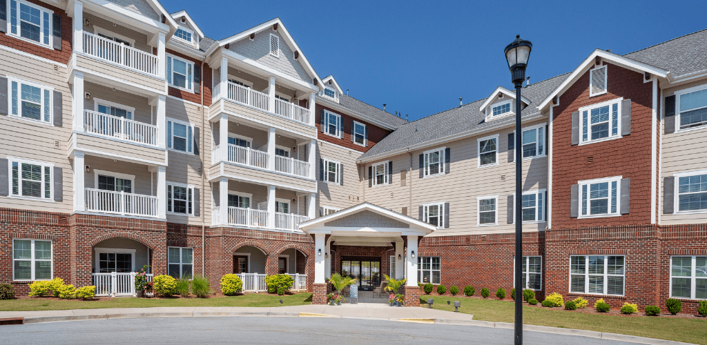 A modern apartment building with multiple balconies and a landscaped entrance under a clear blue sky.