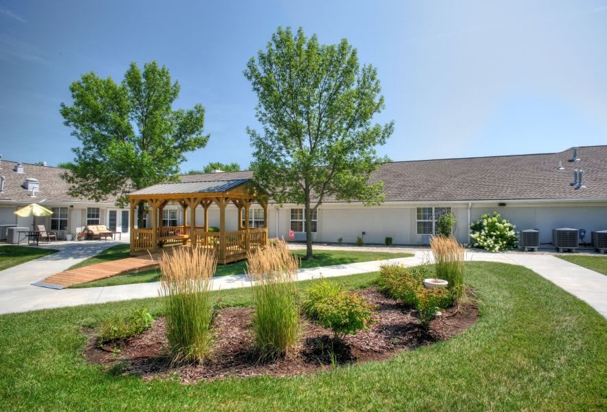 A serene garden with a gazebo and well-maintained landscaping in front of a building on a sunny day.