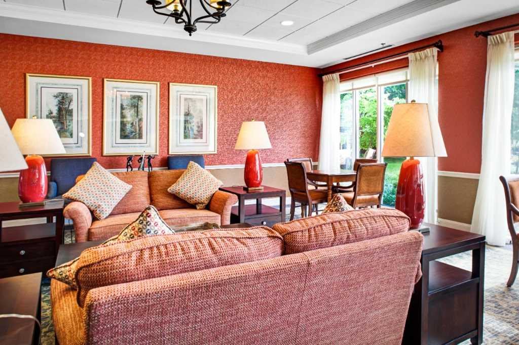 A cozy living room featuring red walls, comfortable sofas, a dining table with chairs, and large windows with natural light.