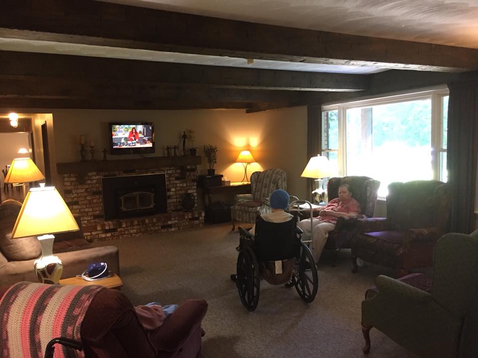 A cozy living room with people watching television, featuring a large window and comfortable seating.