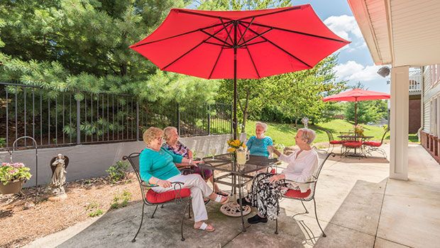 A group of four people sitting under a red patio umbrella, enjoying a conversation in an outdoor setting.