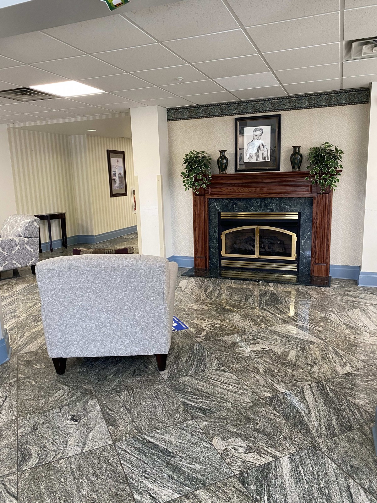 A cozy lobby area featuring a fireplace, armchair, and decorative plants.