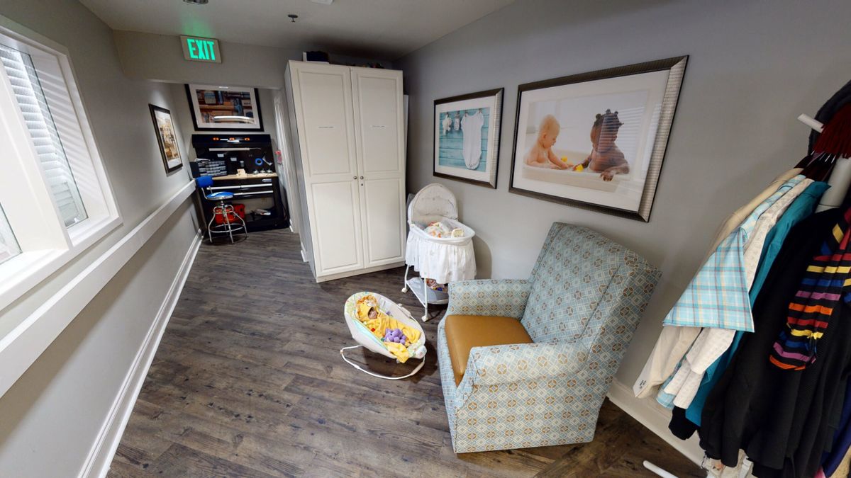 A cozy nursery corner featuring a rocking chair, baby bassinet, and playful artwork.