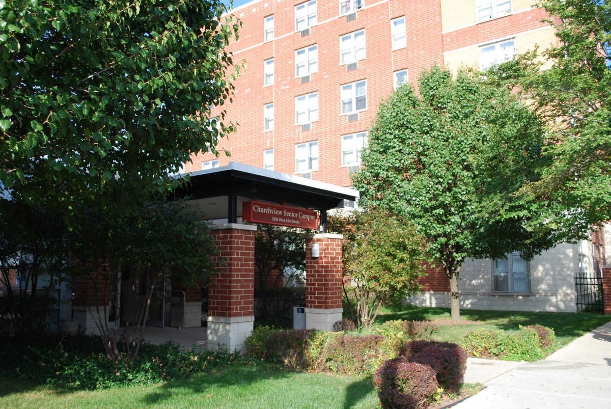 A brick building with a landscaped entrance and surrounding trees.