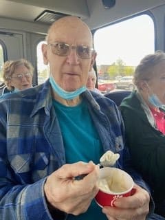 A man wearing glasses and a plaid shirt enjoys ice cream on a bus.