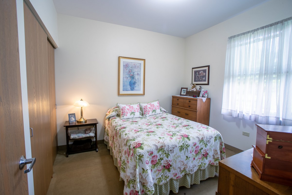 A cozy bedroom with floral bedding, nightstand, and dresser.