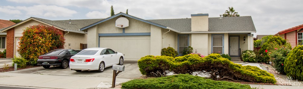 A suburban house with a driveway, featuring a parked car and a basketball hoop above the garage.