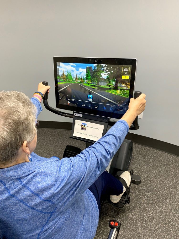 A person using a virtual reality exercise simulator with a road cycling program displayed on the screen.
