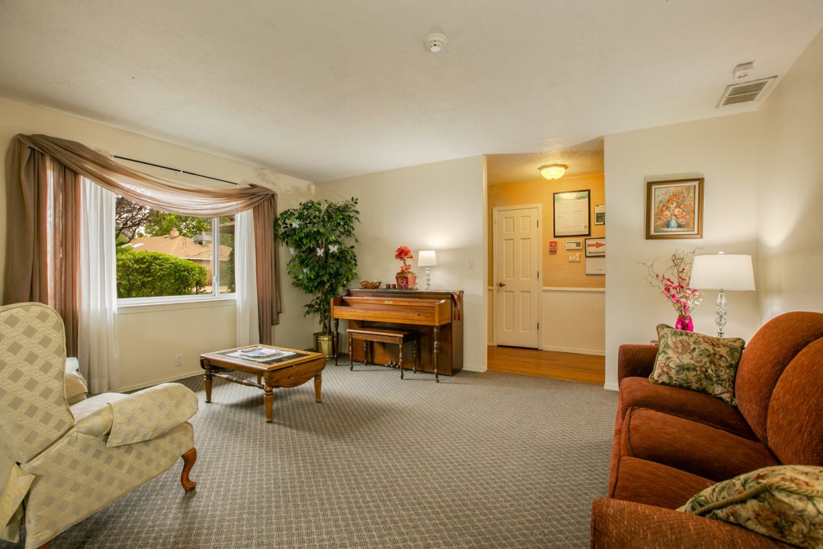 A cozy living room featuring a piano, comfortable seating, and natural light from a large window.